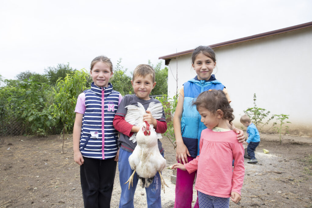 Copii moldoveni care țin un pui în fața casei