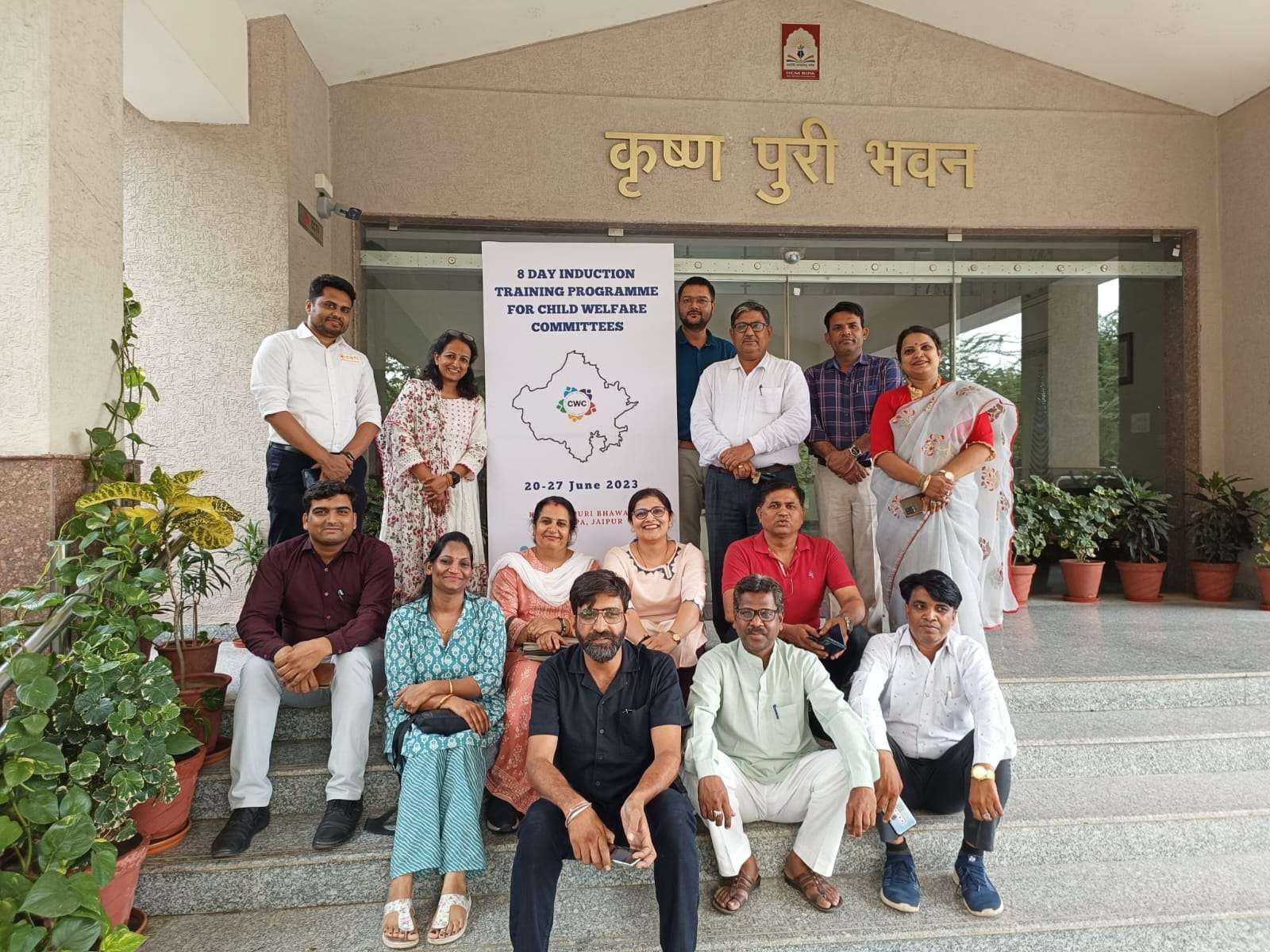 a group of 14 people pose for a photo next to a sign that reads "8 day induction training programme for child welfare committees"